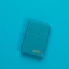 Lifestyle image of Classic Flat Turquoise Zippo Logo Windproof Lighter laying on a turquoise surface