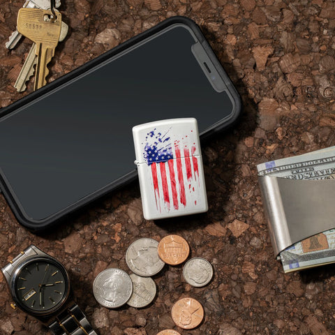 Lifestyle image of US Flag Design White Matte Windproof Lighter laying on a counter top withg a phone, money, keys, and a watch around it.