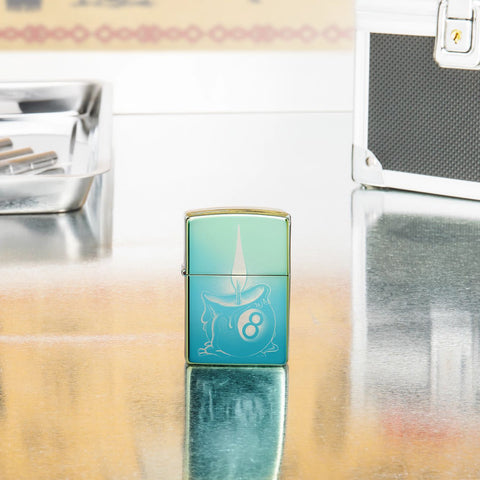 Lifestyle shot of Zippo Eight Ball Tattoo Design High Polish Teal Windproof Lighter standing in on a reflective table with tattoo equipment. 